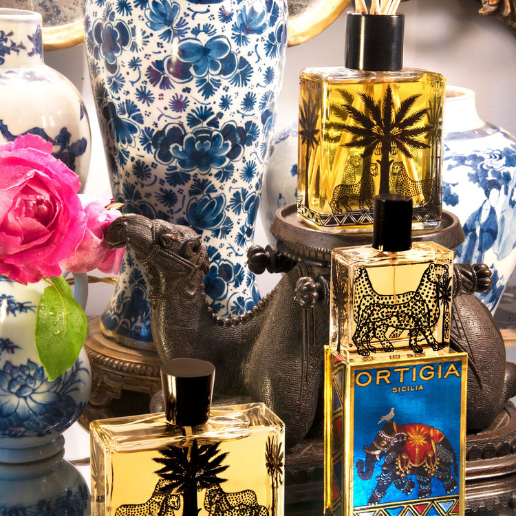 ortigia sandalo perfume bottles of different sizes with a rose and vase in the colourful background