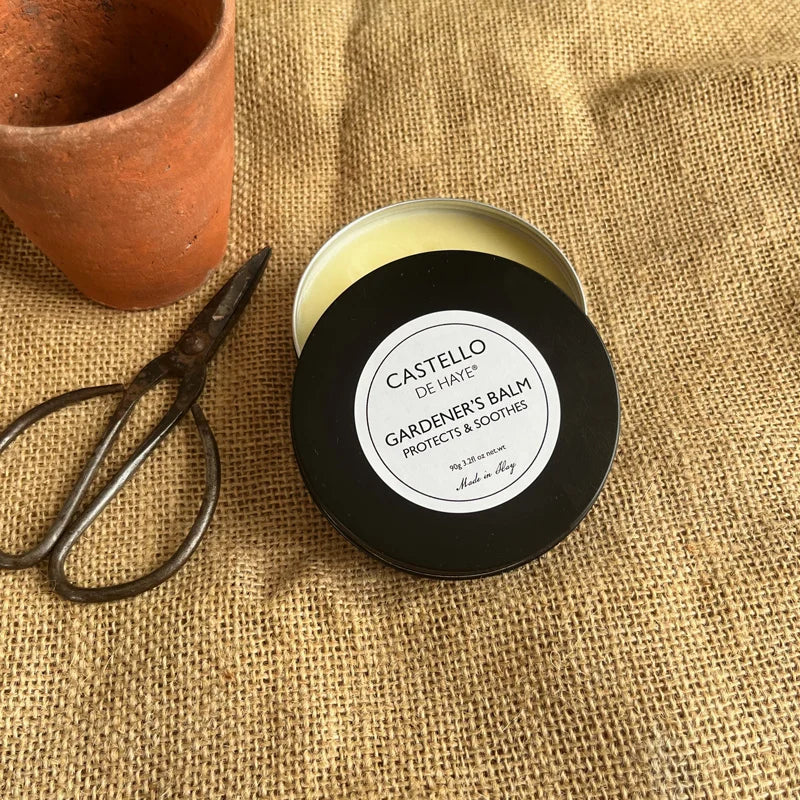 Jar of Castello de Hate Gardeners Balm on a textured fabric background with a pot and scissors.
