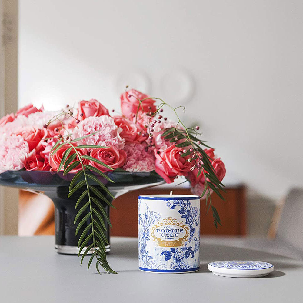 Candle with decorative label next to a bouquet of pink flowers on a table.