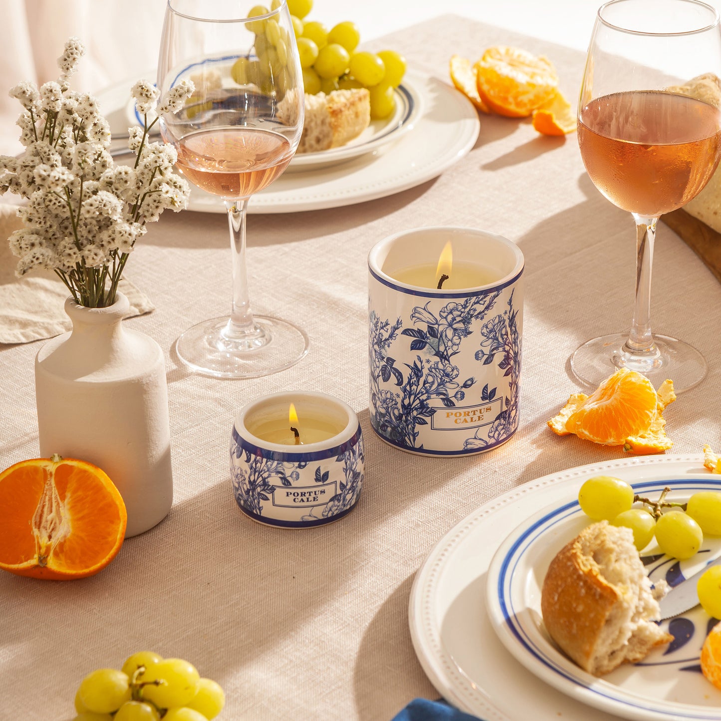 Table setting with candles, wine glasses, and fruit on a light surface