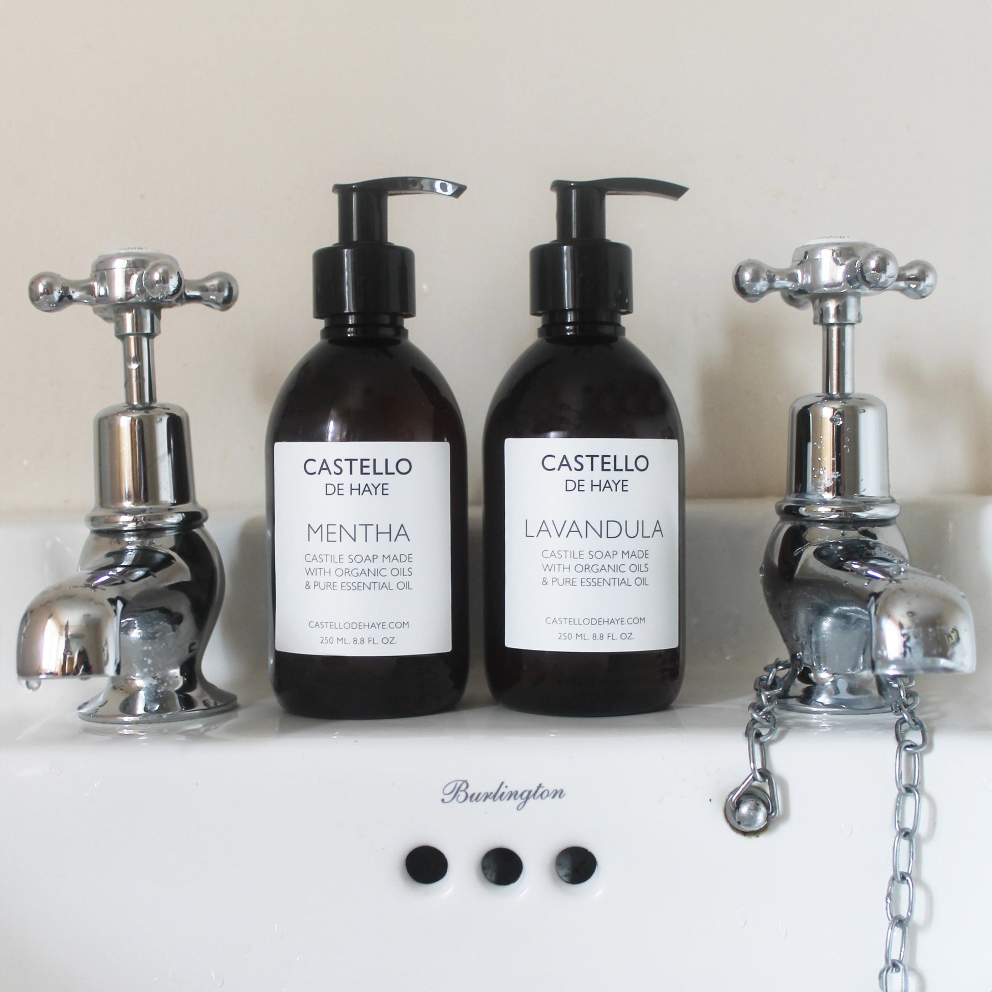 Two bottles of castile soap on a traditional sink between taps